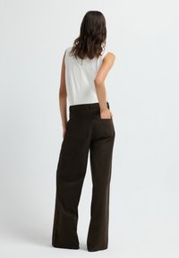 Pantalons marron à jambes larges avec une taille haute, des poches et des boutons sur les côtés. Associés à un haut sans manches blanc, vus de dos.