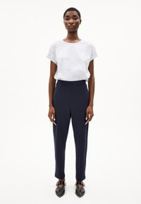 T-shirt bianca a maniche corte abbinata a pantaloni attillati blu navy e ballerine nere con punta appuntita, dotate di cinturino e dettaglio fibbia.