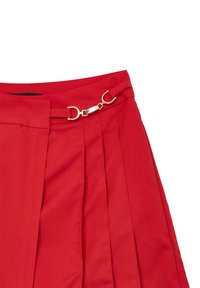 Jupe plissée rouge avec une taille dotée d'une fermeture en métal argenté décorative et de détails de passants de ceinture sur un fond blanc.