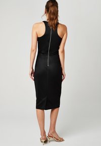 Robe midi en satin noir avec une silhouette ajustée, un design dos nageur et un détail de fermeture éclair central. Présente une fente à l'arrière et une texture lisse.