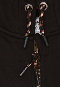 Haut à capuche noir zippé avec cordons tressés, présentant des accents orange, blanc et noir. Comprend une fermeture éclair en métal et une étiquette en tissu à l'intérieur.