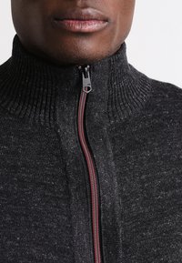 Gray knitted sweater with a high collar, featuring a front zipper with a dark metallic pull and red accent stitching along the zipper.