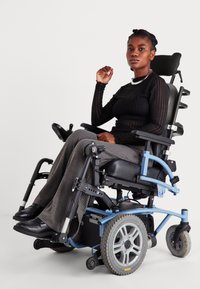 Cadeira de rodas elétrica com um assento e encosto pretos, estrutura azul, rodas cinzas e painel de controlo; utilizador vestido com uma camisa de manga longa preta e calças cinzas.