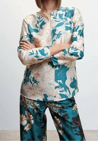 Florale Bluse aus türkis- und beigefarbenem Stoff mit einer Mischung aus großen Blumen und Blättern, durchgehender Knopfleiste und langen Ärmeln.