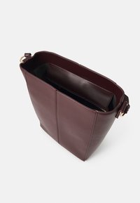 Sac fourre-tout en cuir bordeaux avec une forme structurée, doté d'une ouverture sur le dessus et d'une poche zippée à l'intérieur. Texture lisse et design minimaliste.