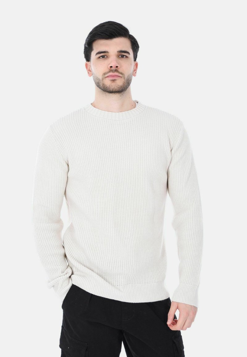 Maglione a maglia di un beige chiaro con texture a coste, scollatura a girocollo e maniche lunghe, abbinato a pantaloni neri.