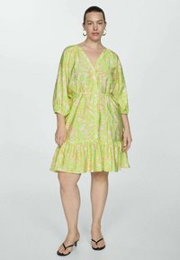 Rochie cu mâneci scurte, decolteu în V, de un verde strălucitor, cu un model floral galben. Fustă evazată cu tiv ondulat și o croială confortabilă. Material ușor.