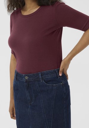 Woman wearing a fitted maroon short-sleeve top tucked into a high-waisted dark blue denim skirt with front seam details.