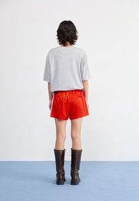 Grijze T-shirt met korte mouwen, rode gestreepte shorts, kniehoge zwarte laarzen. Glad materiaal, ontspannen pasvorm, met een horizontaal streepjespatroon op de shorts.