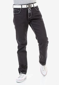 Zwarte spijkerbroek met witte stiksels, voorzakken en een riem met een metalen gesp. Gemaakt in combinatie met witte sneakers.