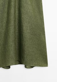 Tessuto verde, dalla texture morbida con un delicato motivo a trama. Il tessuto si drappeggia in modo fluido, presentando un orlo che curva delicatamente nella parte inferiore.