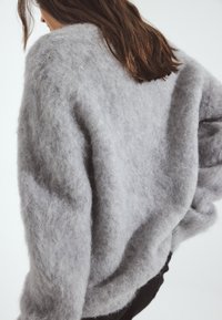 Gray knitted sweater with a fuzzy texture, wide neckline, and dropped shoulders. The fabric appears soft and light, draping loosely.