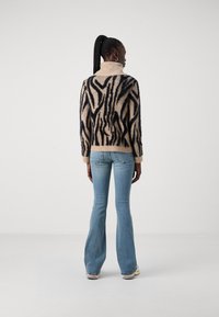 Mönstrad tröja i beige med svarta abstrakta ränder, långa ärmar, hög hals; kombinerad med ljusblå utsvängda jeans.