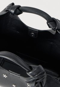 Sac en cuir noir avec une texture extérieure, un intérieur lisse et une poignée supérieure. Comprend une fermeture à bouton-pression et une poche.