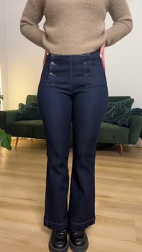 Jeans azul-escuros de cintura subida e com barra alargando, com dois bolsos laterais, quatro botões decorativos na frente e detalhes em costura contrastante.