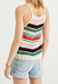 Crochet tílko v pestrých pruzích (červená, zelená, růžová, černá) s vlnkovaným lemem a tenkými ramínky, spárované se světle modrými krátkými kalhotami.