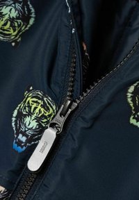 Marinblå jacka med ett iögonfallande tiger mönster. Utrustad med en svart dragkedja som har en slät metallpulltab.