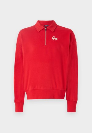 Punainen vetoketjullinen collegepaita, pehmeä rakenne, ribbireunat hihansuissa ja helmassa, jossa on brodeerattu valkoinen "Gap"-logo rinnassa.