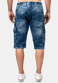 Pantaloni cargo in denim blu sbiadito, con molteplici tasche, dettagli cuciti e un taglio fino al ginocchio. Abbinati a sneakers bianche.