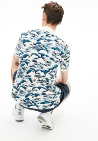 Lyhythihainen poolopaita sinivalkoisella pilvikuosilla, jossa on kaulus ja kirjailtuja yksityiskohtia. Yhdistetty laivastonsinisiin shortseihin ja valkoisiin tennareihin.