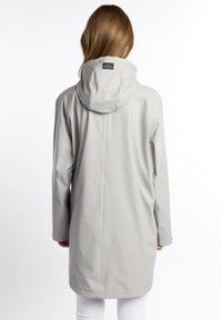 Giacca impermeabile grigio chiaro con cappuccio, texture morbida, maniche lunghe e design lungo fino al ginocchio. Presenta un'etichetta sul retro con dettagli del marchio.