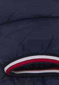 Marine pufferjack met een zachte, quilted textuur. Voorzien van een ronde, gestreepte kraag in rood, wit en blauw.