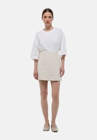 T-shirt blanche oversize, jupe courte de couleur claire et chaussures beige. Design simple avec des textures douces et une coupe décontractée.