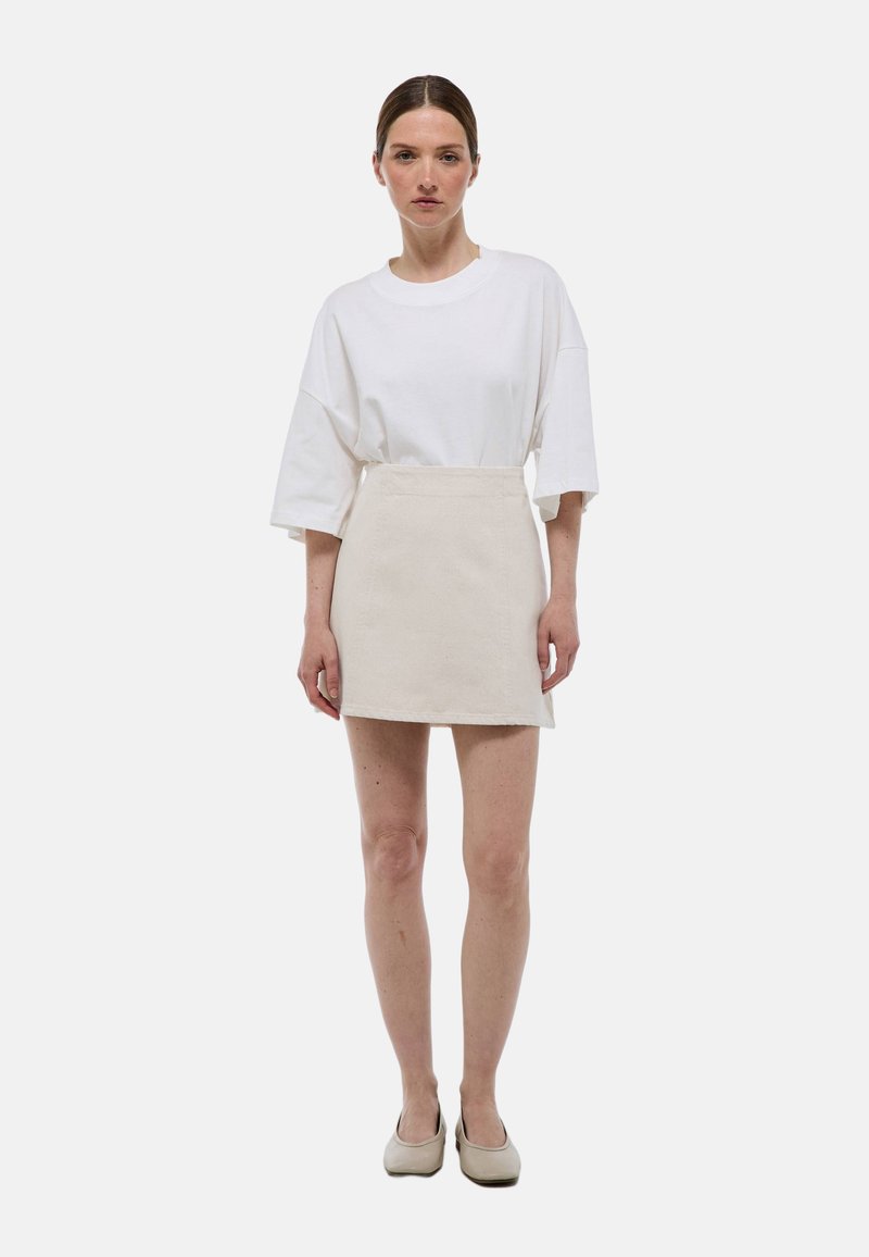 T-shirt blanche oversize, jupe courte de couleur claire et chaussures beige. Design simple avec des textures douces et une coupe décontractée.