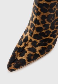Luipaardprint hoge hak schoenen van zacht textiel, met een spitse neus, voorzien van zwarte en bruine vlekken op een tan achtergrond, met een gladde textuur en een strak ontwerp.