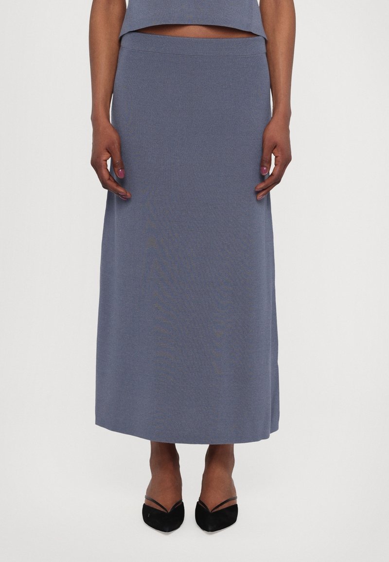 A long, fitted skirt in soft, textured, light blue fabric with a smooth waistband, paired with black pointed-toe shoes.