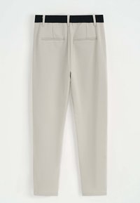 Pantalons slim beige avec une taille élastique noire, dotés de deux poches arrière et d'une texture lisse. Convient pour une tenue formelle ou décontractée.