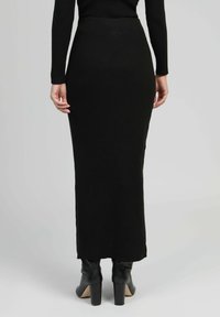 Jupe longue noire en tricot avec une silhouette ajustée, dotée d'une texture côtelée, d'une taille haute et d'une fente sur le côté, associée à des bottines à talons noires.