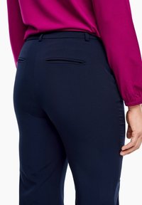Pantalon bleu marine avec une finition en tissu lisse, doté de deux poches arrière et d'un design subtilement ajusté. Associé à un chemisier à manches longues fuchsia.