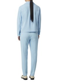 Jasnoniebieski zestaw marynarki i spodni wykonany z gładkiego, tkane materiału. Marynarka ma kołnierz i zapięcia na guziki; spodnie są skrojone na miarę.
