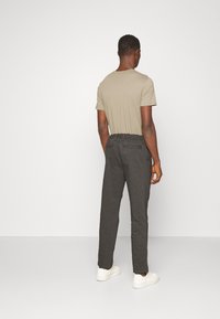 En khaki t-shirt och mörkgrå byxor med elastiskt midjeband, visade bakifrån. Vita sneakers fulländar outfitten.