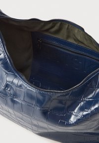 Sötétkék, krokodilbőr hatású bőr táska cipzárral. A belső rész sötét szövetbéléssel és cipzáras zsebbel rendelkezik a tárolásra.