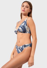 Niebieski i kremowy bikini w wzory z trójkątnym stanikiem z przednim węzłem oraz pasującymi niskimi majtkami, o gładkiej fakturze i żywym wzornictwie.