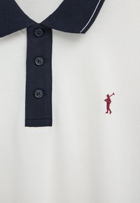 Polo blanco con cuello y tapeta de botones en azul marino, con un pequeño logo bordado en granate de un jugador de polo en el pecho.