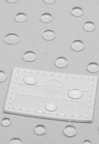Texturerad grått tyg med vattendroppar. Har en vit rektangulär etikett präglad med "JOHNNY URBAN" och cirkulära logodetaljer.