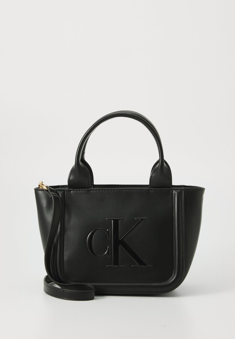 Borsa a tracolla in pelle nera con logo "cK" in rilievo. Presenta manici corti e una tracolla regolabile. Tessuto liscio, forma strutturata.