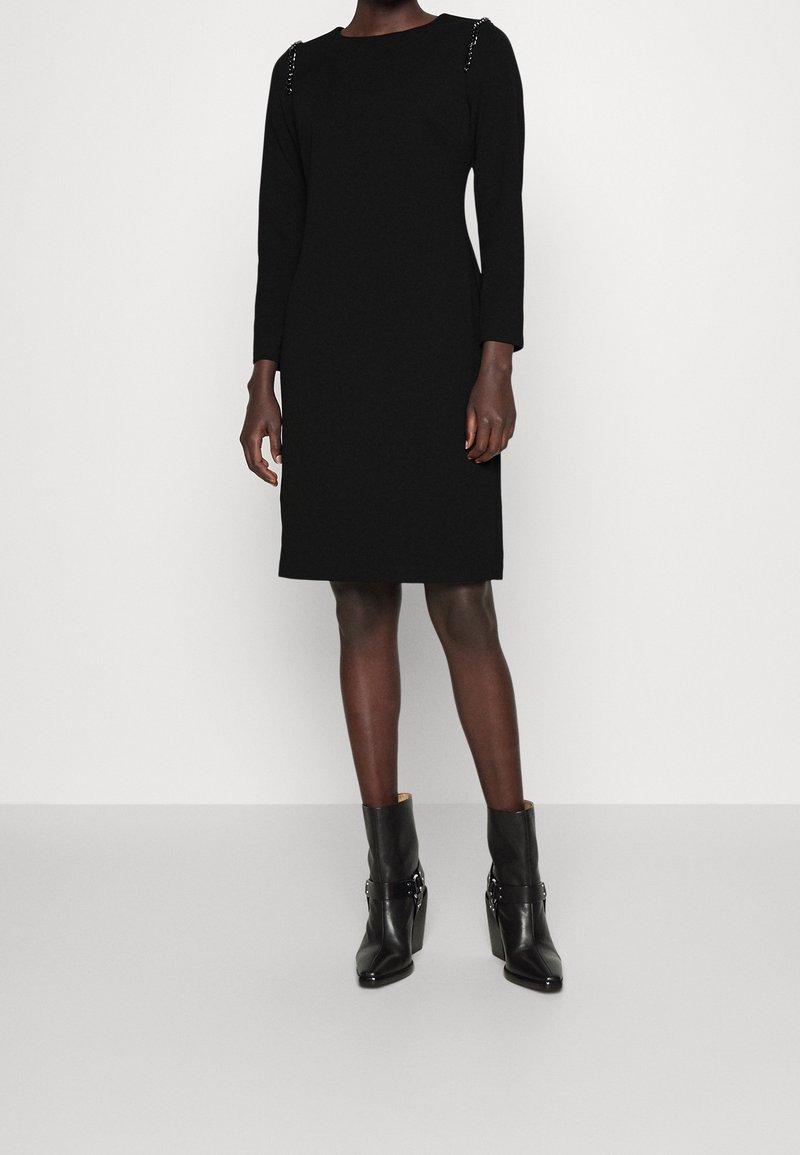 Černé dlouhé šaty s rovnými liniemi, ozdobené detaily na ramenou. V kombinaci s černými vysokými botami na kotníku.