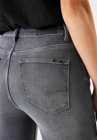 Grijze denim jeans met een hoge taille, twee achterzakken en een subtiele logopatch. De stof heeft een gladde, licht gestructureerde afwerking.