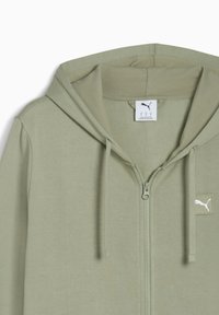 Lys grøn zip-up hoodie med snoretræk i hætten, blødt stof og et lille hvidt logo-patch på venstre bryst. Lynlås-lukningen har en metallisk detalje.