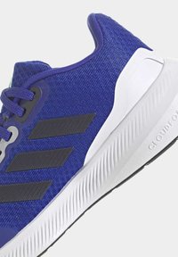 Scarpa sportiva blu con tomaia in tessuto texturizzato, logo a tre strisce nere e suola bianca texturizzata con motivo a onde.