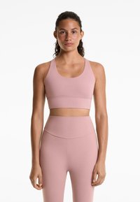 Roze sport-beha met brede bandjes en een ronde halslijn, gecombineerd met high-waisted leggings in dezelfde kleur en met een gladde textuur.