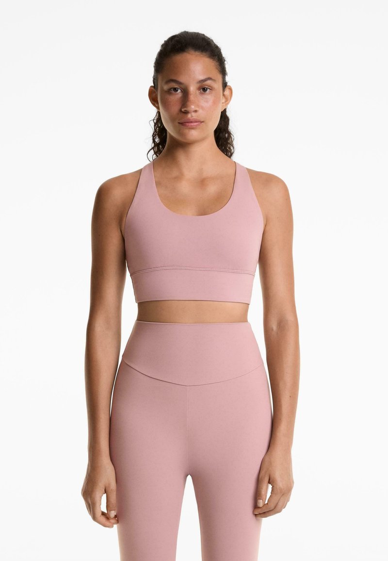 Roze sport-beha met brede bandjes en een ronde halslijn, gecombineerd met high-waisted leggings in dezelfde kleur en met een gladde textuur.