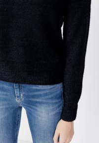 Pulover negru pufos cu mâneci lungi, guler rotund și tiv cu dantelă. Asortat cu blugi din denim albastru, cu un design clasic cu cinci buzunare.