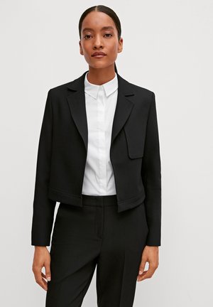 Schwarze, gekürzte Blazerjacke mit strukturierten Revers, offener Vorderseite und langen Ärmeln, über einem weißen Kragenhemd getragen. Glattes Material und taillierte Passform.