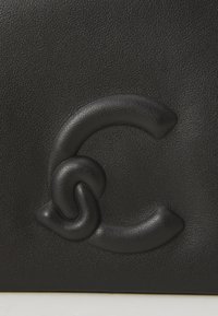 Black leather bag featuring a textured surface and a prominent intertwined "C" logo. The design emphasizes a smooth and glossy finish.