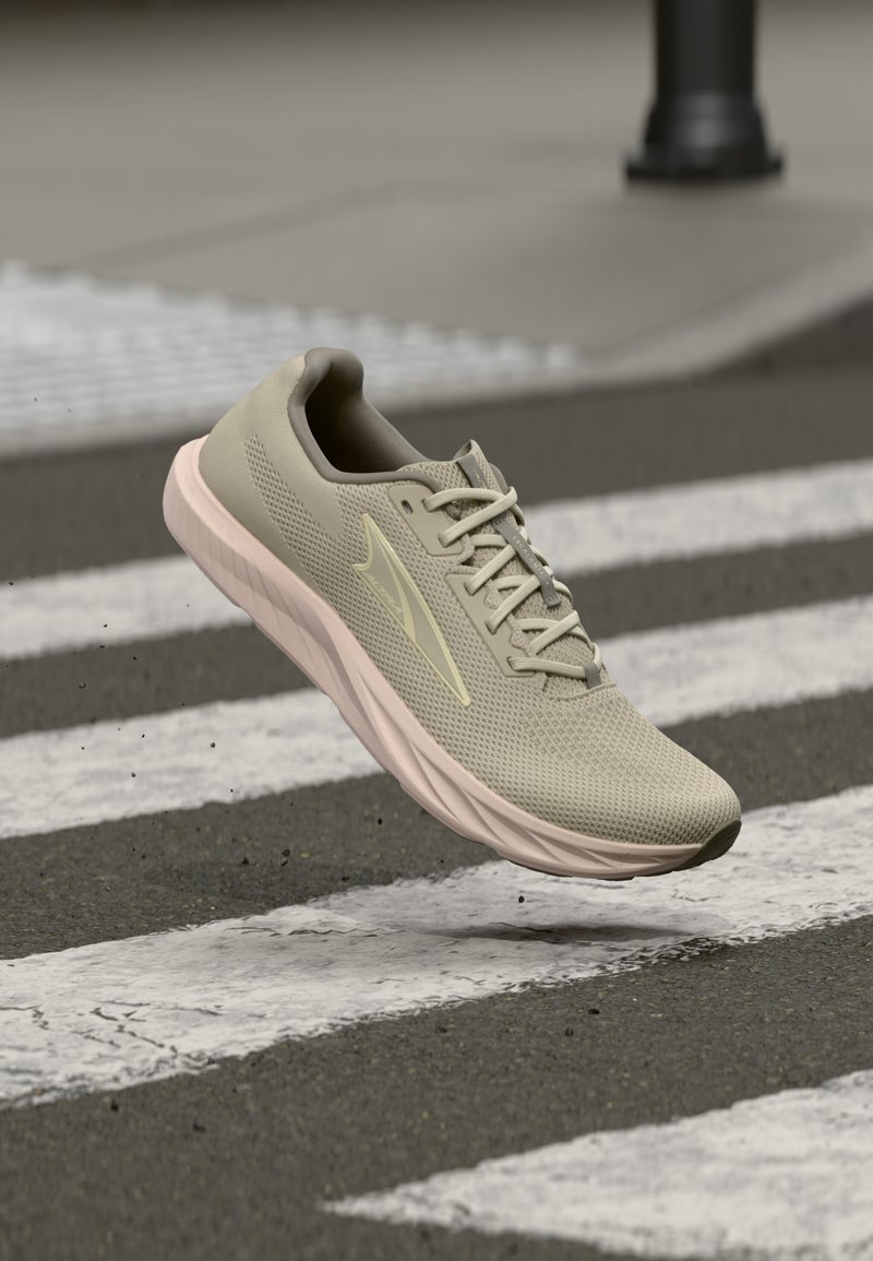 Αθλητικό παπούτσι ανοιχτού μπεζ χρώματος με επάνω μέρος από δίχτυ και παχιά σόλα, να αιωρείται πάνω από διάβαση πεζών σε άσφαλτο.